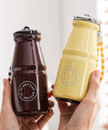 Коричневий і жовтий термоси «Milk Bottle» у формі пляшки для молока в руках